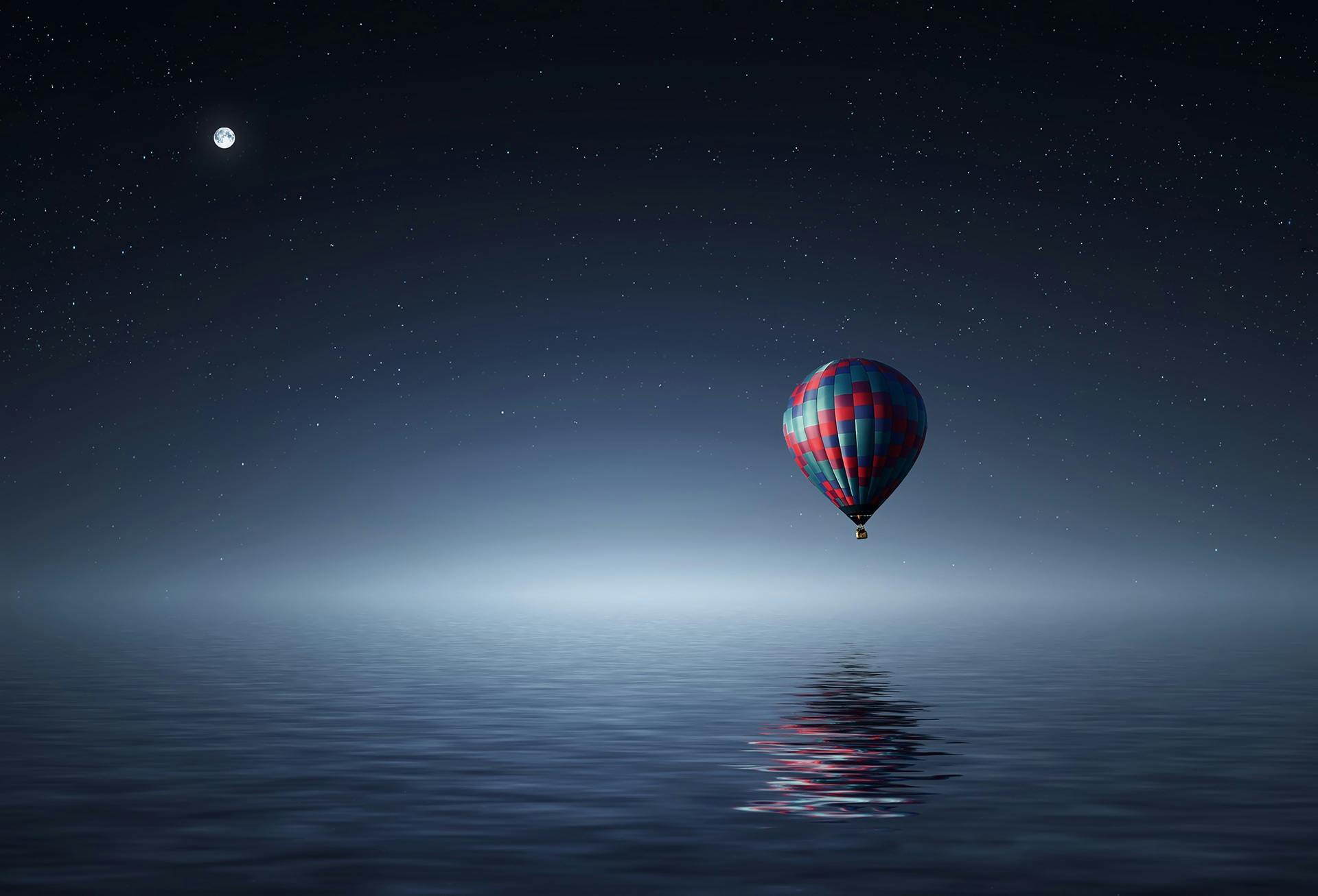 A balloon floating over water on a clear starry night